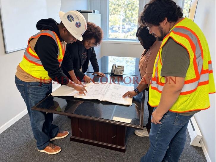 JOADEM inspectors in safety vests and a hard hat reviewing construction drawings around a conference table